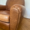 Gros plan d'un fauteuil Paire de fauteuils Club 1940 marron usé sur un plancher en bois près d'un mur blanc. Brocante 93
