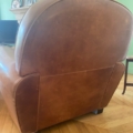 La Paire de fauteuils Club 1940 en cuir marron est posée sur un plancher en bois, vue de derrière, avec des murs verts et une cheminée en arrière-plan. Brocante 93