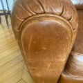 Gros plan d'un accoudoir en cuir marron usé sur la Paire de fauteuils Club 1940, présentant des rayures et des plis visibles rappelant les fauteuils club vintage. Brocante 93