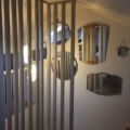 Un couloir avec des lattes de bois verticales, des lampes suspendues et le Miroir biseauté 1950 à côté de miroirs vintage sur un mur blanc. Brocante 93