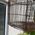 Gros plan sur une cage à oiseaux rouillée Cage déco jard suspendue près d'une fenêtre et de plantes vertes, apportant un charme vintage à votre décor de jardin. Brocante 93