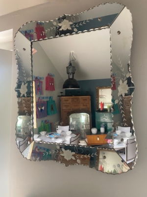 Le Miroir biseauté 1950 représente une salle à manger avec une table dressée et des serviettes colorées au mur, apportant un charme vintage au décor. Brocante 93