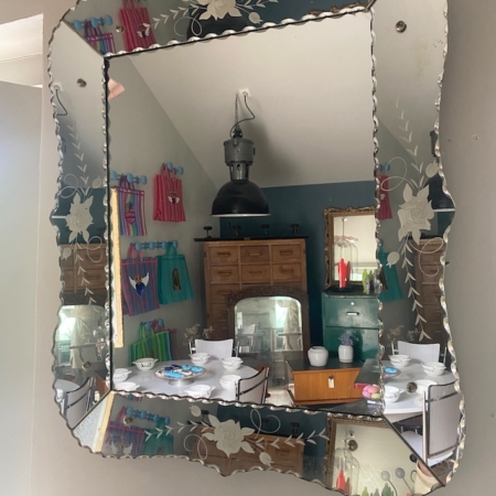 Le Miroir biseauté 1950 représente une salle à manger avec une table dressée et des serviettes colorées au mur, apportant un charme vintage au décor. Brocante 93