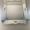 Le Miroir biseauté 1950, un miroir rectangulaire dont les bords sont ornés de motifs floraux vintage, est fixé sur un mur de couleur claire. Brocante 93