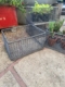 Un panier métallique des Caisses industrielles 1960 et des plantes en pot reposent sur un patio en béton ; le panier vide au premier plan ajoute un charme à la décoration vintage. Brocante 93