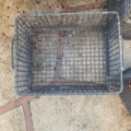 Le panier rectangulaire en fil de fer des Caisses industrielles de 1960 repose sur une surface en béton, avec des pétales de fleurs rouges éparpillés à proximité. Brocante 93