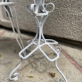 Pied de table en métal blanc avec des boucles, design décoratif sur un patio en pierre près d'un mur texturé. Brocante 93