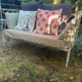 Lit en fer forgé 1950 stylisé comme un banc en fer vintage, associé à la Tour Eiffel et à des coussins à pois, placé dans un jardin entouré de verdure. Brocante 93