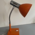 La Lampe articulée 1970 en orange et argent, dotée d'un col flexible, repose sur une surface bleu-gris contre un mur blanc. Brocante 93