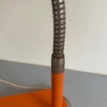 Gros plan d'un collier de lampe en métal flexible fixé à la base orange de la Lampe articulée 1970 sur une surface grise, évoquant le style vintage classique. Brocante 93