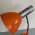 La Lampe articulée 1970 en orange et argent, dotée d'un col flexible, est exposée sur une surface grise contre un mur blanc. Brocante 93