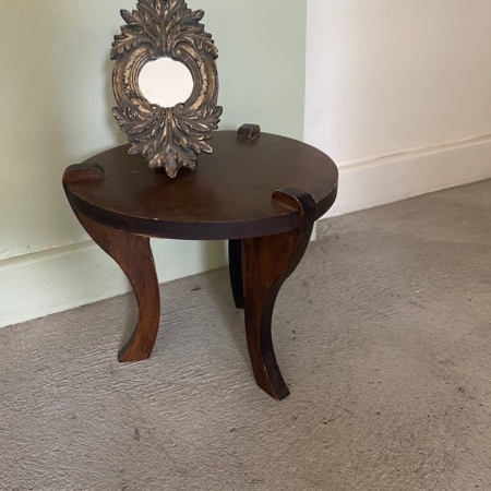 Une petite table ronde en bois aux pieds incurvés accueille un cadre photo ovale vide et orné, tandis que le Repose pieds 1960 est posé à proximité. Brocante 93