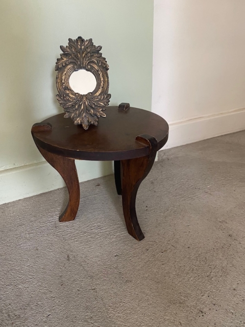 Une petite table ronde en bois aux pieds incurvés accueille un cadre photo ovale vide et orné, tandis que le Repose pieds 1960 est posé à proximité. Brocante 93