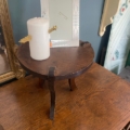 Une bougie blanche avec une étoile dorée est posée sur une petite table ronde en bois, à côté du Repose pieds 1960, avec un miroir et des photos en arrière-plan. Brocante 93