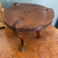 Une petite table ronde en bois avec trois pieds courbés est posée sur une surface en bois contre un mur bleu, évoquant le style de la collection Repose pieds 1960. Brocante 93