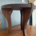 Le Repose pieds 1960 est un petit repose-pieds en bois foncé avec trois pieds courbés, présenté sur une surface en bois près d'un mur bleu. Brocante 93
