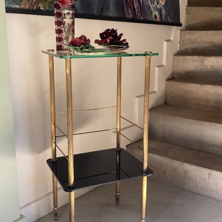 Une table d'appoint Sellette verre et laiton de 1950 avec des garnitures dorées et un décor floral rouge se trouve à côté d'un escalier en béton et d'un tableau de plumes de paon. Brocante 93