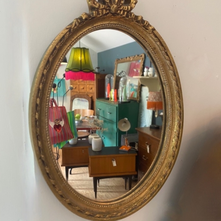 Le Miroir ovale 1950 ajoute un charme vintage à une pièce animée par des lampes colorées, des armoires rétro et des meubles élégants des années 1950. Brocante 93