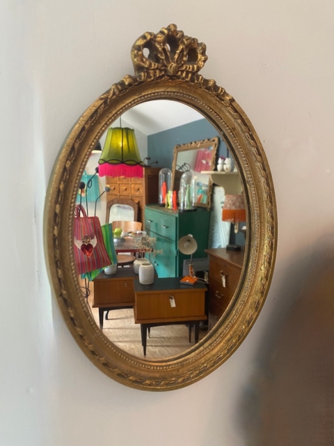 Le Miroir ovale 1950 ajoute un charme vintage à une pièce animée par des lampes colorées, des armoires rétro et des meubles élégants des années 1950. Brocante 93