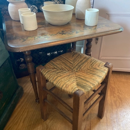 Petite table en bois avec tasses et bols en céramique, à côté d'un charmant Tabouret paille vintage 1960 avec siège tressé, posé sur un sol en bois. Brocante 93