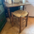 Une petite table en bois avec des bols en céramique et un Tabouret paille vintage 1960, associée à une chaise à assise tressée sur un sol en bois. Brocante 93