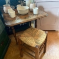 Petite table rustique avec des poteries et des vases à côté d'un Tabouret paille vintage 1960 sur un sol en bois. Brocante 93