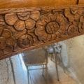 Des détails floraux en bois sculpté surmontent le trumeau Miroir 1940 vieilli et moucheté, reflétant subtilement les chaises situées en dessous. Brocante 93