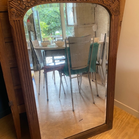 Le Miroir trumeau 1940, avec son cadre en bois ancien, reflète les chaises de salle à manger et la table dans une pièce ensoleillée dotée d'une fenêtre donnant sur le jardin. Brocante 93