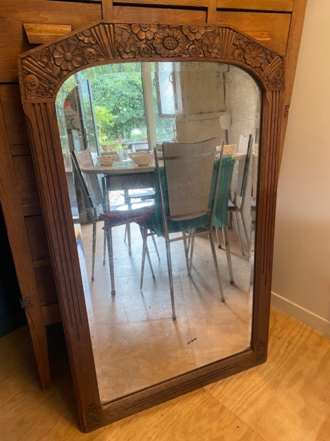 Le Miroir trumeau 1940, avec son cadre en bois ancien, reflète les chaises de salle à manger et la table dans une pièce ensoleillée dotée d'une fenêtre donnant sur le jardin. Brocante 93