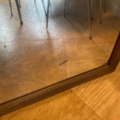 Le Miroir trumeau 1940 avec un cadre en bois reflète les pieds d'une chaise en métal sur un sol en bois. Brocante 93