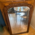 Un Miroir trumeau 1940 avec un cadre en bois orné reflète une table et des chaises dans une pièce confortable, insufflant un charme vintage à l'espace. Brocante 93