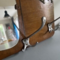 Gros plan sur la peinture murale Porte-manteaux 1940, avec des crochets métalliques et un petit miroir qui reflète une pièce lumineuse - évoquant l'élégance vintage. Brocante 93