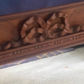 Gros plan sur le Miroir noeud PM 1940, qui présente une sculpture en bois ornée d'un ruban noeud, au-dessus d'un sol gris et d'un tapis à motifs. Brocante 93