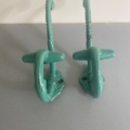 La Paire de patères 1930 turquoise en forme d'ancres évoque le style vintage, posée sur une surface gris clair avec un fond blanc. Brocante 93