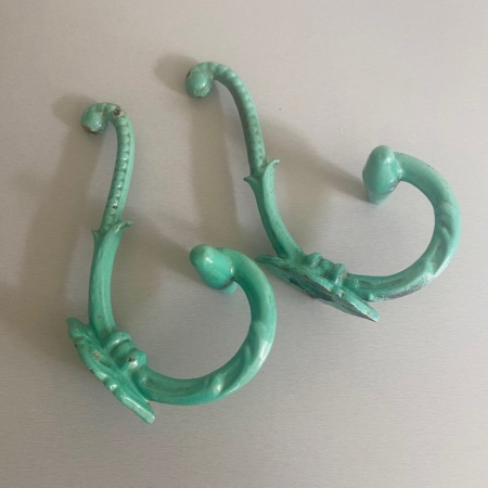 Deux crochets en métal vert et orné - Paire de patères 1930 - au design vintage reposent sur une surface gris clair. Brocante 93
