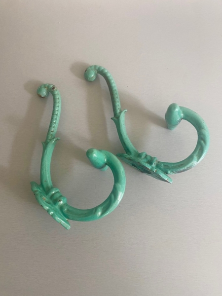 Deux crochets en métal vert et orné - Paire de patères 1930 - au design vintage reposent sur une surface gris clair. Brocante 93