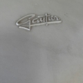 Un logo métallique "Gautier" orne la surface gris clair subtilement texturée de la Chaise Gautier 1970, capturant son charme vintage. Brocante 93