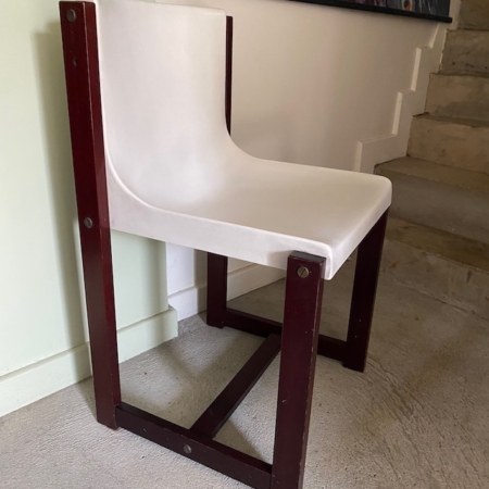 La Chaise Gautier 1970, avec son assise blanche incurvée et son cadre en bois foncé, se trouve près de l'escalier et d'un mur orné d'œuvres d'art. Brocante 93