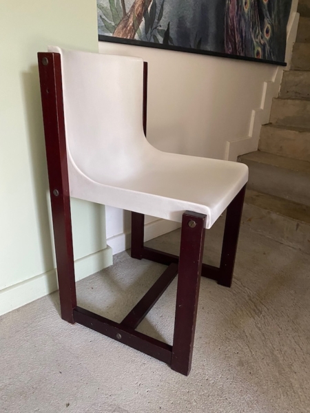 La Chaise Gautier 1970, avec son assise blanche incurvée et son cadre en bois foncé, se trouve près de l'escalier et d'un mur orné d'œuvres d'art. Brocante 93