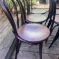 Quatre Lot de chaises bistrot au bois foncé et aux dossiers incurvés sont disposés en rang sur une terrasse en bois à l'extérieur, créant ainsi une charmante installation parfaite pour les repas en plein air. Brocante 93