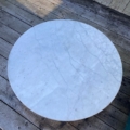 La Table basse début XXème siècle, une table ronde en marbre blanc, est posée sur une terrasse en bois usée par le temps et la lumière du soleil. Brocante 93