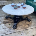 La Table basse début XXème siècle, avec un plateau rond en marbre et un pied griffe noir, présente cinq petits vases avec des fleurs séchées sur une terrasse en bois. Brocante 93