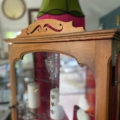 Vitrine murale vintage 1950 en bois avec portes vitrées, exposant verrerie et bougie, surmontée d'un abat-jour vert. Brocante 93