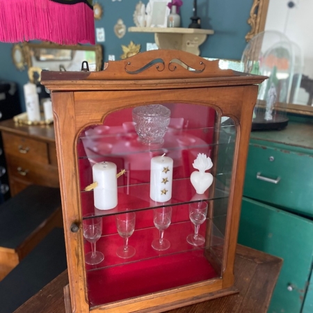Une Vitrine murale vintage 1950 présente des bougies et de la verrerie, élégamment disposées sur une table dans une charmante pièce de style rétro. Brocante 93