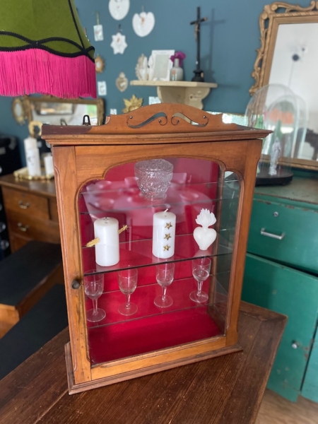 Une Vitrine murale vintage 1950 présente des bougies et de la verrerie, élégamment disposées sur une table dans une charmante pièce de style rétro. Brocante 93