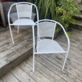 Une paire de fauteuils de jardin blancs est placée sur une terrasse en bois, entourée de plantes verdoyantes et de marches accueillantes. Brocante 93