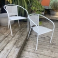 Une paire de fauteuils de jardin blancs est installée sur une terrasse en bois à l'extérieur, entourée de plantes vertes. Brocante 93
