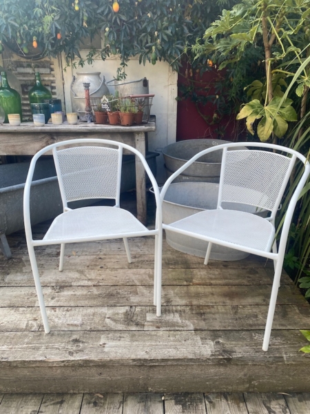 La paire de fauteuils de jardin blancs en métal, placée sur une terrasse en bois et entourée de plantes, offre un espace convivial et idéal pour profiter du plein air. Brocante 93