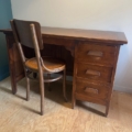 Un bureau vintage de 1960 avec trois tiroirs et une chaise en bois assortie sont posés sur un sol en bois clair contre un mur uni, apportant un charme vintage à la pièce. Brocante 93
