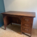 Un Bureau vintage 1960 avec trois tiroirs à droite est posé sur un sol en bois contre un mur blanc. Brocante 93